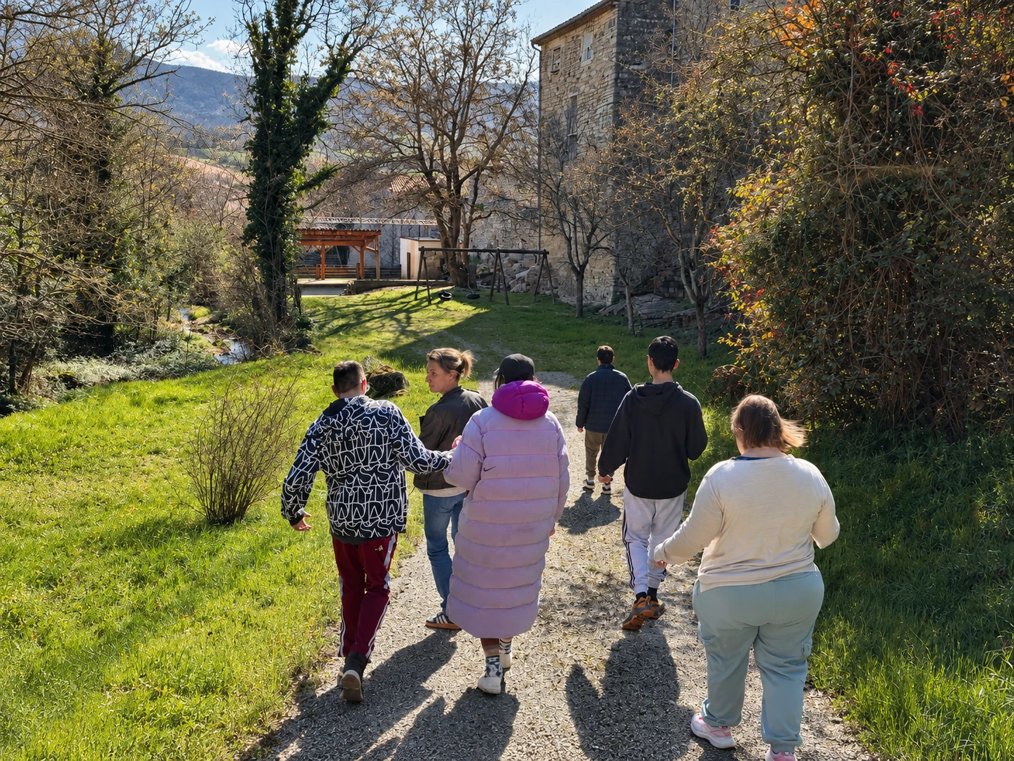Un groupe marche ensemble sur un chemin bordé de verdure et de bâtiments en pierre.